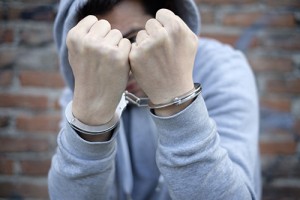 portrait of handcuffed young man with face hidden by sweatshirt hood